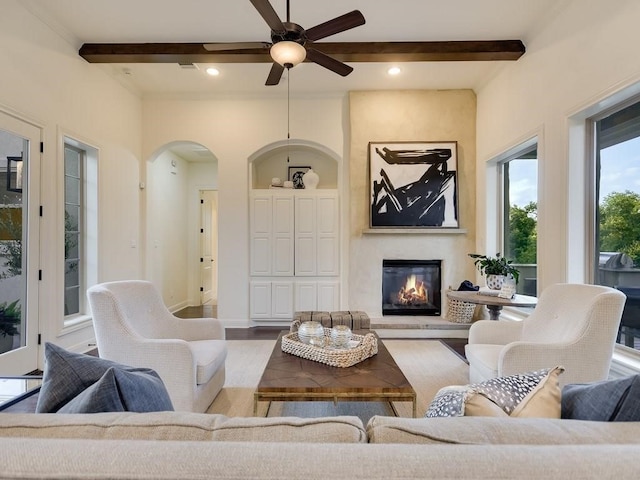 living room featuring ceiling fan, a large fireplace, wood-type flooring, and beam ceiling