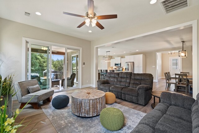 living room with ceiling fan with notable chandelier and hardwood / wood-style flooring