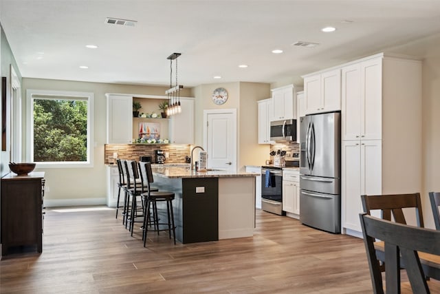 kitchen with light hardwood / wood-style flooring, tasteful backsplash, white cabinets, a kitchen bar, and appliances with stainless steel finishes