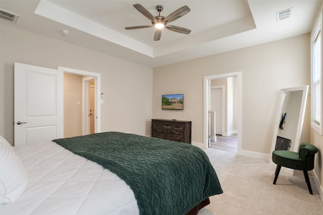 bedroom with light carpet, ceiling fan, and a raised ceiling