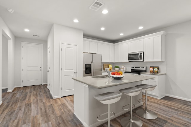 kitchen featuring white cabinets, a center island with sink, appliances with stainless steel finishes, and a kitchen breakfast bar