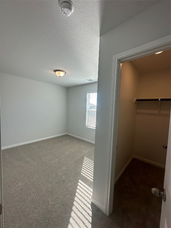 interior space with carpet flooring, a spacious closet, a closet, and a textured ceiling