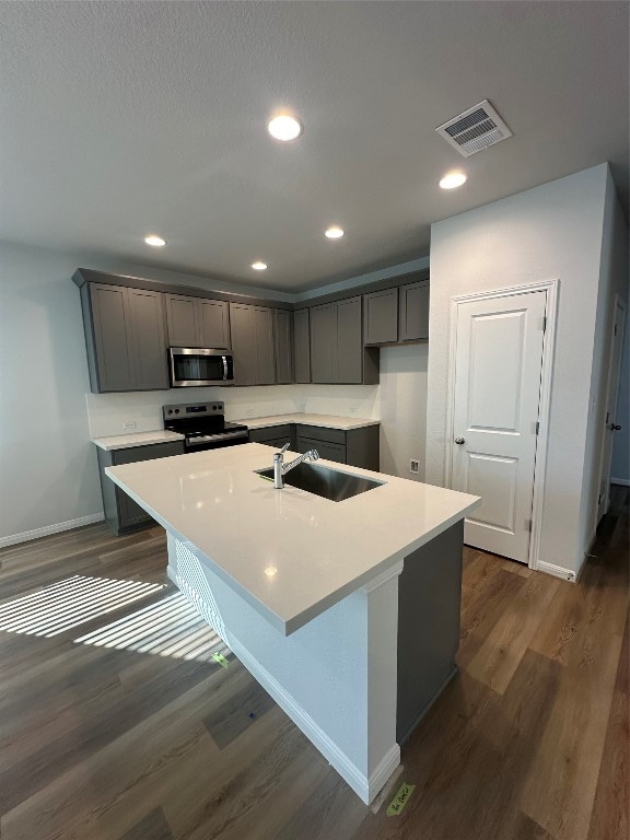 kitchen with an island with sink, stainless steel appliances, dark wood-type flooring, and sink