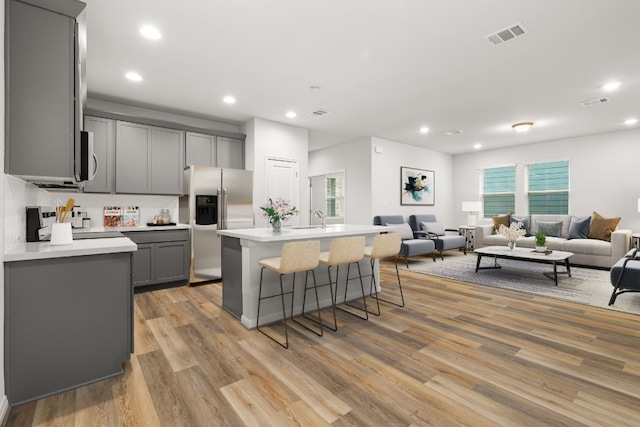 kitchen featuring stainless steel refrigerator with ice dispenser, a kitchen breakfast bar, gray cabinets, and an island with sink