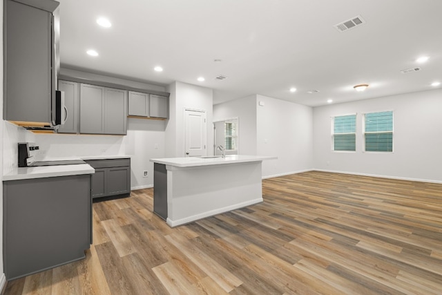 kitchen with a kitchen island with sink, gray cabinetry, range, and light hardwood / wood-style floors