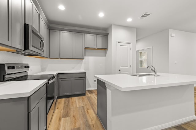 kitchen featuring gray cabinets, sink, light hardwood / wood-style floors, stainless steel appliances, and a center island with sink