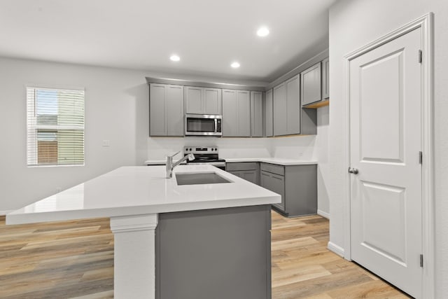 kitchen featuring gray cabinets, appliances with stainless steel finishes, sink, a kitchen island with sink, and light wood-type flooring