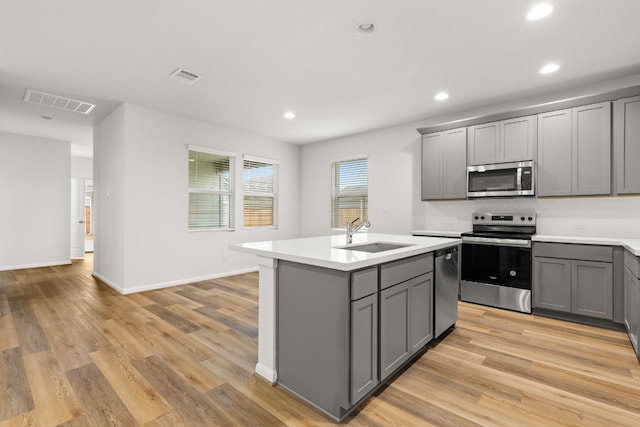 kitchen featuring sink, gray cabinetry, appliances with stainless steel finishes, an island with sink, and light hardwood / wood-style floors