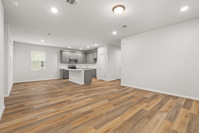 kitchen with a kitchen island, gray cabinetry, light wood-type flooring, and appliances with stainless steel finishes