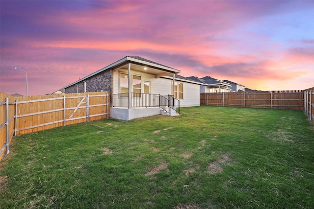 back house at dusk featuring a lawn