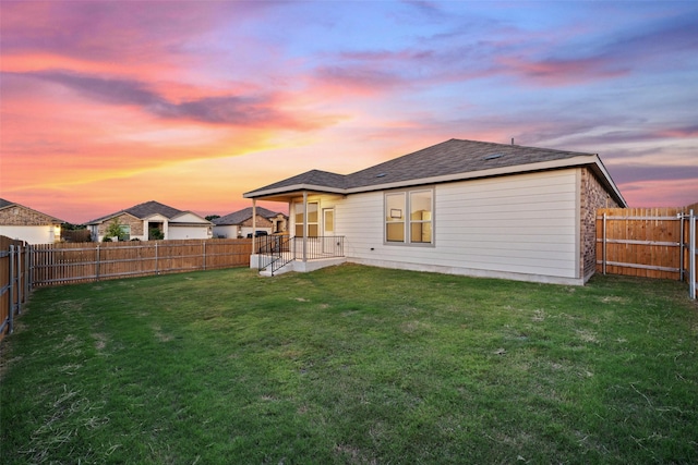 back house at dusk featuring a lawn