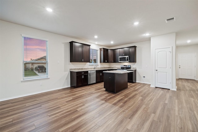 kitchen featuring light wood-type flooring, stainless steel appliances, dark brown cabinetry, a center island, and sink