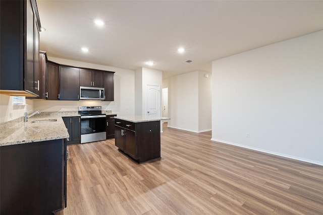 kitchen featuring stainless steel appliances, light stone counters, light hardwood / wood-style floors, a kitchen island, and sink