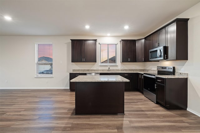 kitchen with wood-type flooring, a center island, stainless steel appliances, dark brown cabinets, and light stone countertops