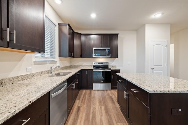 kitchen with appliances with stainless steel finishes, sink, light hardwood / wood-style flooring, light stone counters, and dark brown cabinets