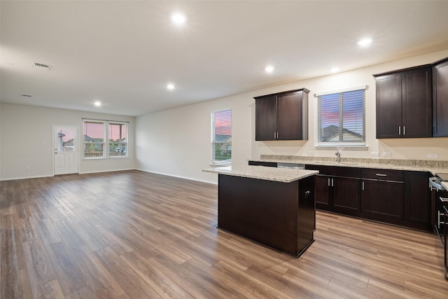 kitchen featuring dark brown cabinets, light stone countertops, a center island, and light hardwood / wood-style floors