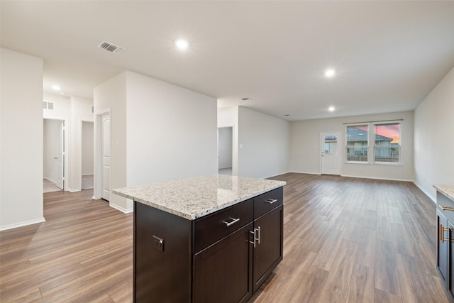 kitchen with light wood-type flooring, a kitchen island, light stone countertops, and dark brown cabinets