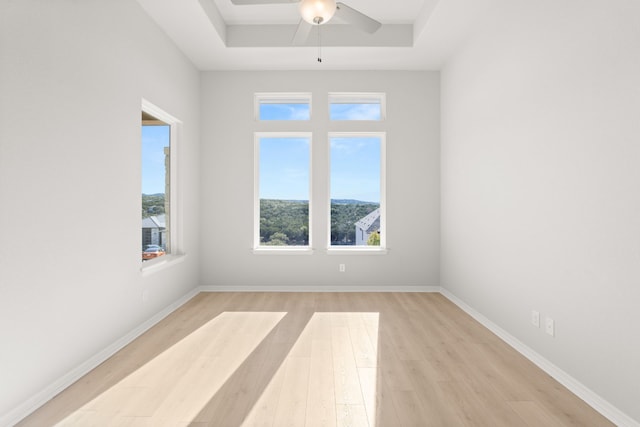 empty room featuring light hardwood / wood-style floors, a raised ceiling, plenty of natural light, and ceiling fan