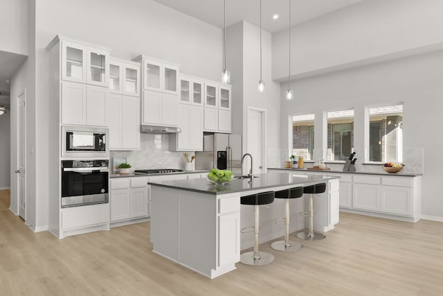 kitchen with white cabinets, pendant lighting, a towering ceiling, and stainless steel appliances