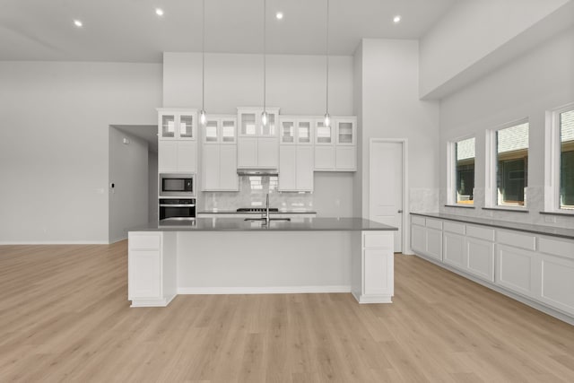 kitchen featuring built in microwave, sink, oven, pendant lighting, and white cabinets