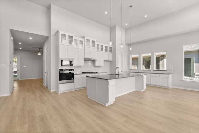 kitchen with stainless steel appliances, white cabinetry, hanging light fixtures, and a kitchen island with sink