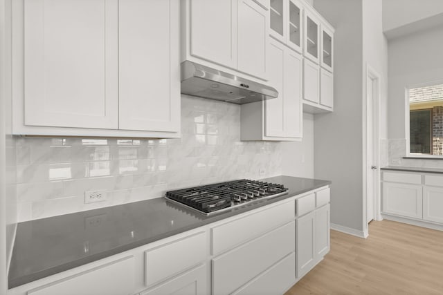 kitchen featuring stainless steel gas stovetop, white cabinets, light wood-type flooring, tasteful backsplash, and extractor fan