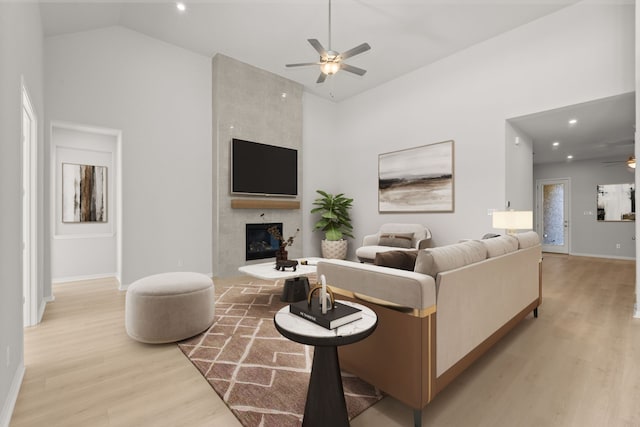 living room with ceiling fan, a fireplace, high vaulted ceiling, and light hardwood / wood-style flooring