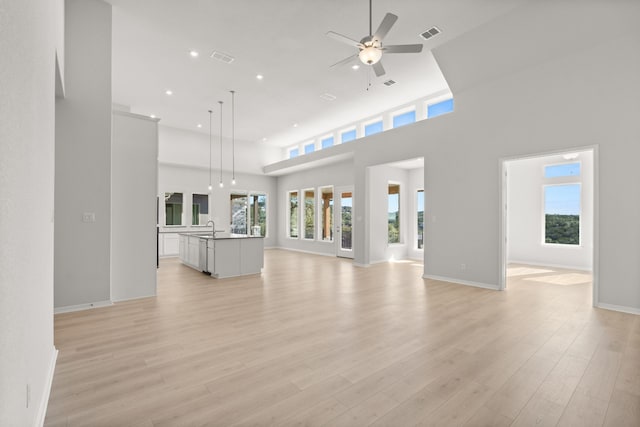 unfurnished living room featuring a high ceiling, light hardwood / wood-style flooring, ceiling fan, and sink