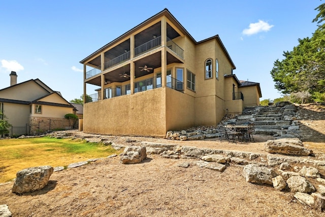 view of side of property with ceiling fan, fence, a balcony, and stucco siding