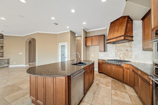 kitchen featuring visible vents, dark stone countertops, stainless steel appliances, premium range hood, and a sink