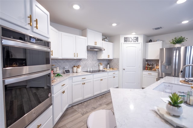 kitchen featuring appliances with stainless steel finishes, white cabinetry, light stone countertops, and tasteful backsplash