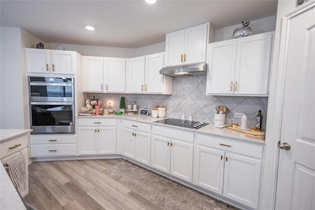 kitchen with light hardwood / wood-style flooring, white cabinets, double oven, black electric cooktop, and tasteful backsplash