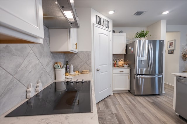 kitchen featuring light hardwood / wood-style flooring, backsplash, white cabinetry, wall chimney exhaust hood, and appliances with stainless steel finishes