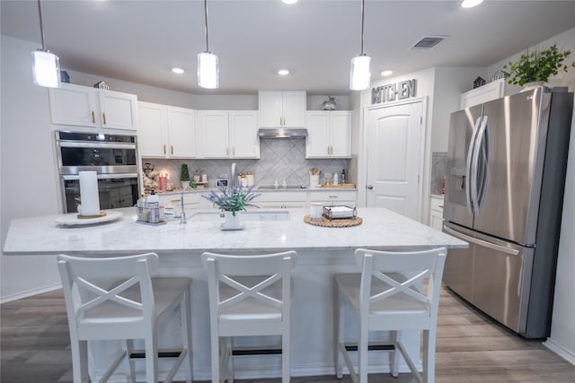 kitchen featuring hardwood / wood-style flooring, tasteful backsplash, an island with sink, stainless steel appliances, and a breakfast bar area