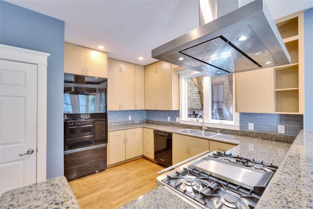 kitchen with cream cabinets, island exhaust hood, light hardwood / wood-style flooring, appliances with stainless steel finishes, and light stone countertops