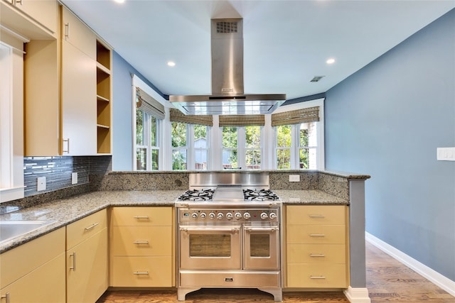 kitchen featuring wall chimney exhaust hood, a wealth of natural light, light stone counters, and range with two ovens