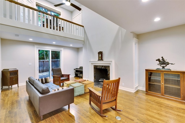 living room featuring a high end fireplace, light hardwood / wood-style floors, ceiling fan, and a towering ceiling