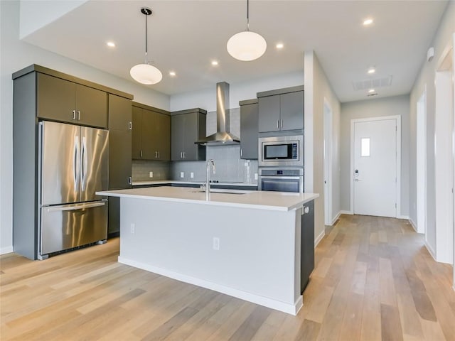 kitchen featuring a kitchen island with sink, wall chimney range hood, light hardwood / wood-style flooring, tasteful backsplash, and stainless steel appliances