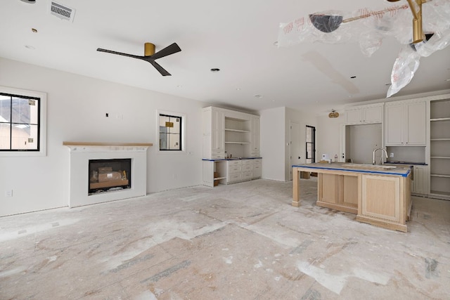 kitchen with a glass covered fireplace, visible vents, an island with sink, and open shelves