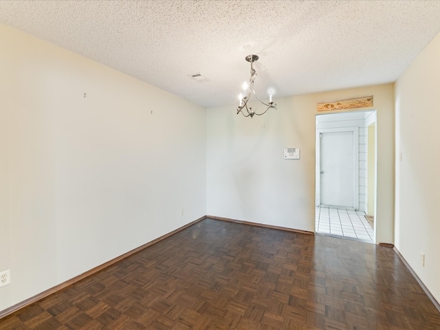 empty room with an inviting chandelier, a textured ceiling, and dark parquet flooring