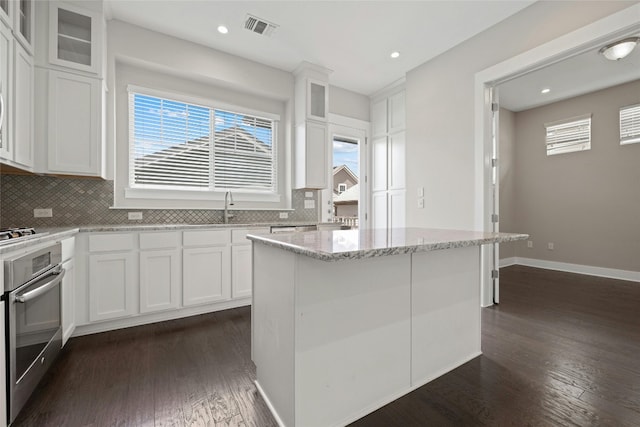 kitchen featuring dark hardwood / wood-style floors, tasteful backsplash, a center island, white cabinets, and appliances with stainless steel finishes