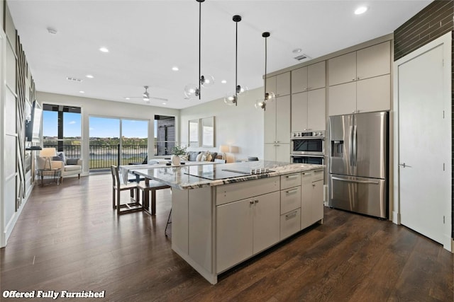 kitchen featuring a center island, ceiling fan, light stone counters, appliances with stainless steel finishes, and dark hardwood / wood-style flooring