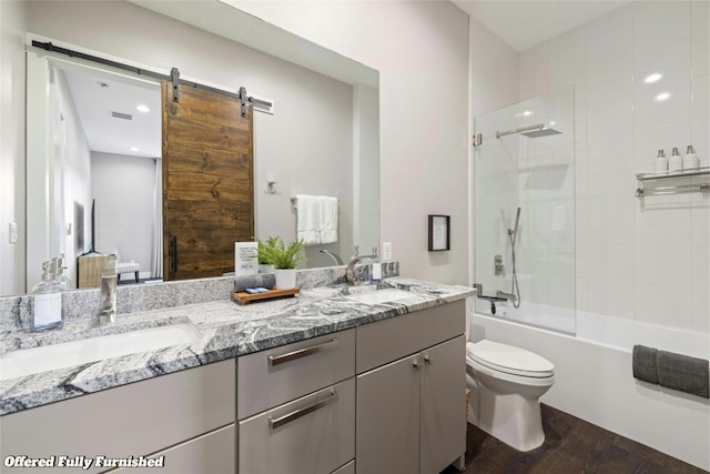 full bath featuring double vanity, bath / shower combo with glass door, a sink, and wood finished floors