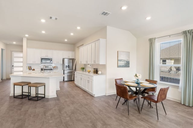 kitchen featuring appliances with stainless steel finishes, recessed lighting, light countertops, a sink, and an island with sink
