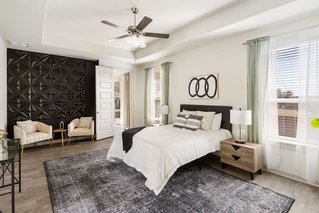 bedroom featuring visible vents, a raised ceiling, an accent wall, and wood finished floors