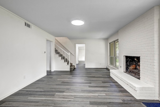 unfurnished living room with a brick fireplace, stairs, visible vents, and wood finished floors