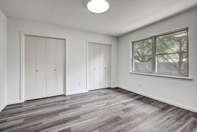 unfurnished bedroom featuring wood finished floors, baseboards, and two closets