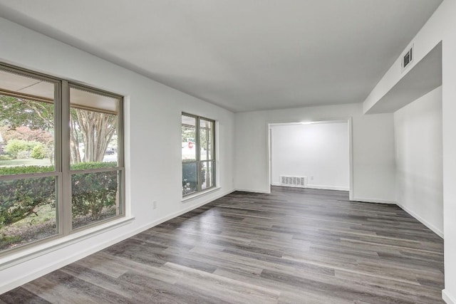 empty room with dark wood-style floors, baseboards, and visible vents