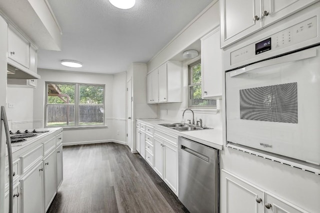 kitchen featuring white appliances, a sink, white cabinets, light countertops, and dark wood finished floors