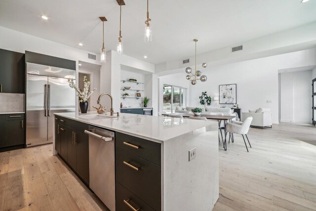 kitchen with sink, built in features, an island with sink, decorative light fixtures, and stainless steel appliances